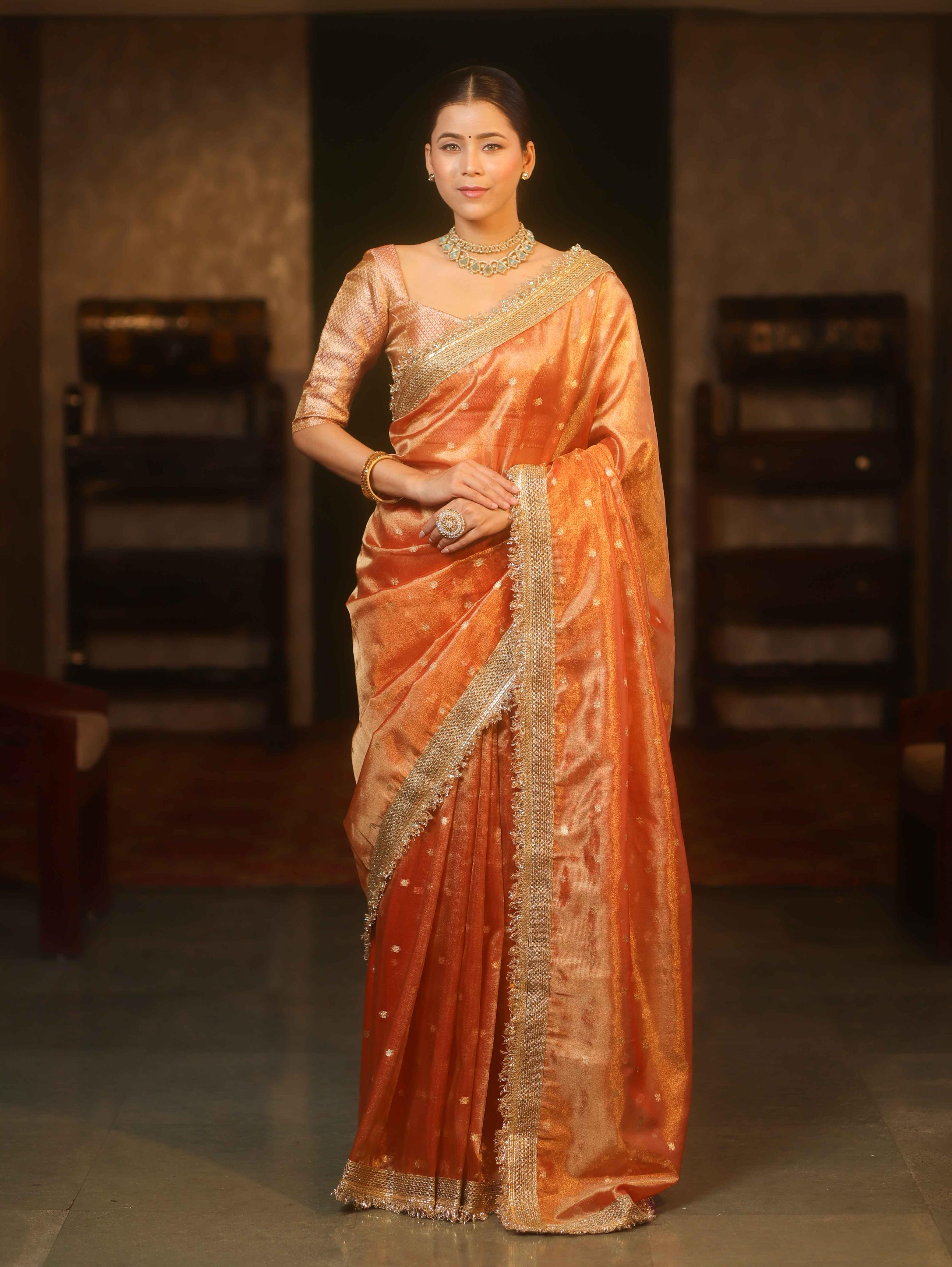 Folded coral peach Tissue Organza Banarasi saree showing floral pallu, zari border and fringe detailing