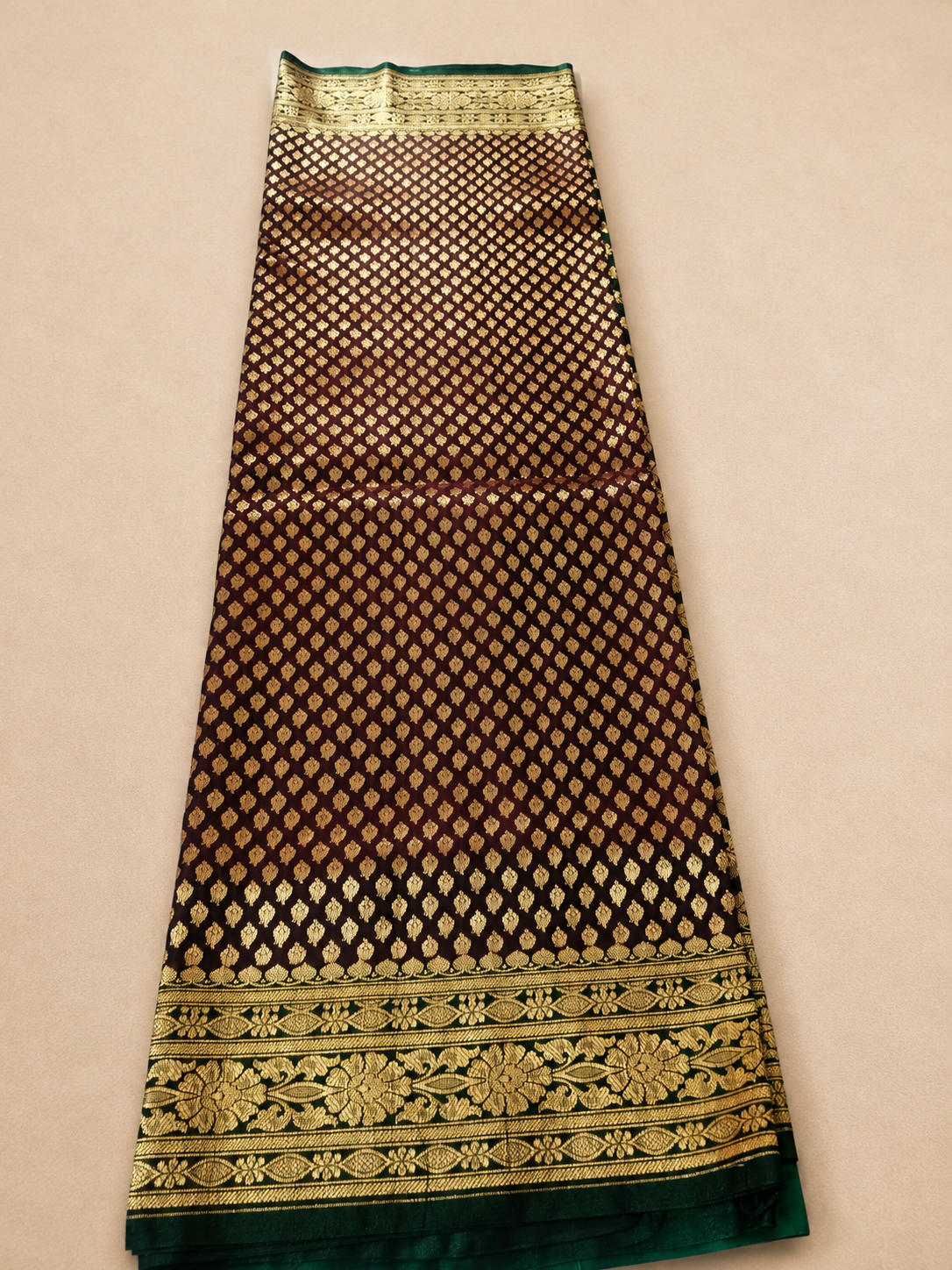 Deep maroon Banarasi silk saree – full open flat lay showing dense all-over gold booti pattern and wide woven gold floral vine border with green edge