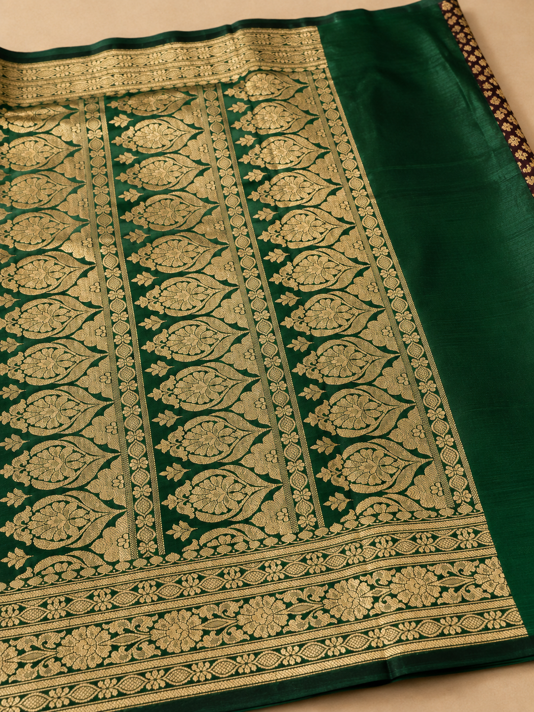 Deep maroon Banarasi silk saree – contrast dark green pallu close-up showing large gold woven leaf teardrop motifs with floral fill in vertical panel arrangement