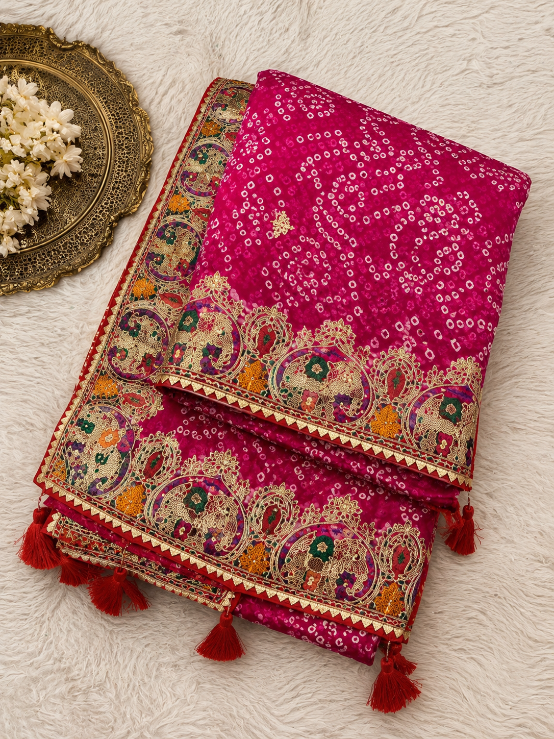 Rani pink bandhani georgette saree – folded flat lay showing all-over bandhani pattern, wide paisley border and red tassels